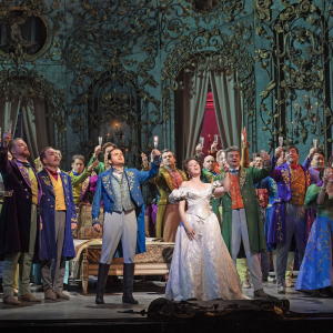 an image of the company in the Act One party scene with Violetta in the centre, they are making a toast.