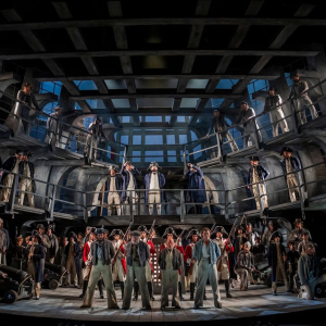 An image of the full company of the opera facing forwards on the set of a ship.